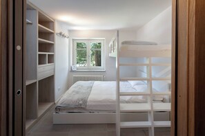 A bedroom with a bunk bed, a wooden wardrobe, a window with a view of trees, and a radiator. - Maison Rue de La Neige - Family Escape (Valtournanche Aosta)