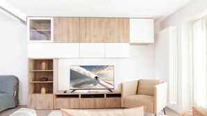 Ein modernes Wohnzimmer mit Flachbildfernseher, Holzschränken, einer Couch und einem Sessel.