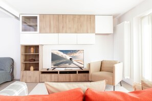 Ein modernes Wohnzimmer mit Flachbildfernseher, Holzschränken, einer Couch und einem Sessel.