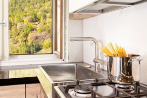 Eine Küche mit Fenster, Spüle aus Edelstahl und einem Topf Spaghetti auf dem Herd.