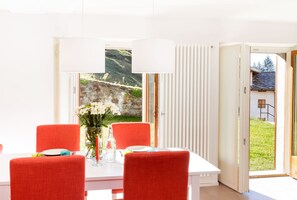 Ein Essbereich mit Tisch, Stühlen und Blick auf eine gebirgige Landschaft durch ein großes Fenster.