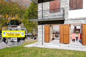 A stone building with wooden shutters, a balcony, and a sign indicating nearby locations. - Maison Rue de La Neige - Family Escape (Valtournanche Aosta)