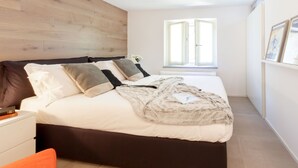 Ein Schlafzimmer mit einem Bett, einem Nachttisch, einem Fenster und einer Wand mit Holzverkleidung.
