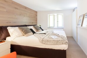 Ein Schlafzimmer mit einem Bett, einem Nachttisch, einem Fenster und einer Wand mit Holzverkleidung.