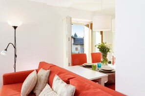 A modern living room with a red sofa, a white table, and a dining area with chairs and a vase of flowers. - Maison Rue de La Neige - Family Escape (Valtournanche Aosta)