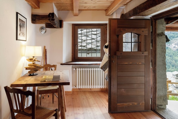 Une pièce aux murs en bois, avec une table, des chaises, une fenêtre donnant sur un paysage et une porte.