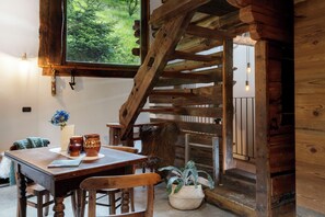 Interior rústic de fusta amb taula de dinar, cadires, una escala i vistes a la vegetació.