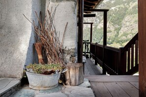 Zona exterior rústica amb un terraç de fusta, una jardinera metàl·lica amb plantes i una cornisa de pedra.