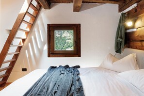 A bedroom with a wooden ladder, a window with a view of trees, a bed with white linens, and a green towel hanging on the wall. - Chalet da MiRo - Authentic Rascard & Scenic View (Valtournanche Aosta)