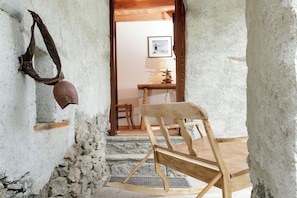 Un intérieur rustique avec un fauteuil à bascule en bois, un mur en pierre et un tableau encadré accroché au mur.