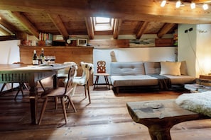 Une pièce chaleureuse avec un plafond en bois, un canapé, une table à manger avec des chaises et une bibliothèque.