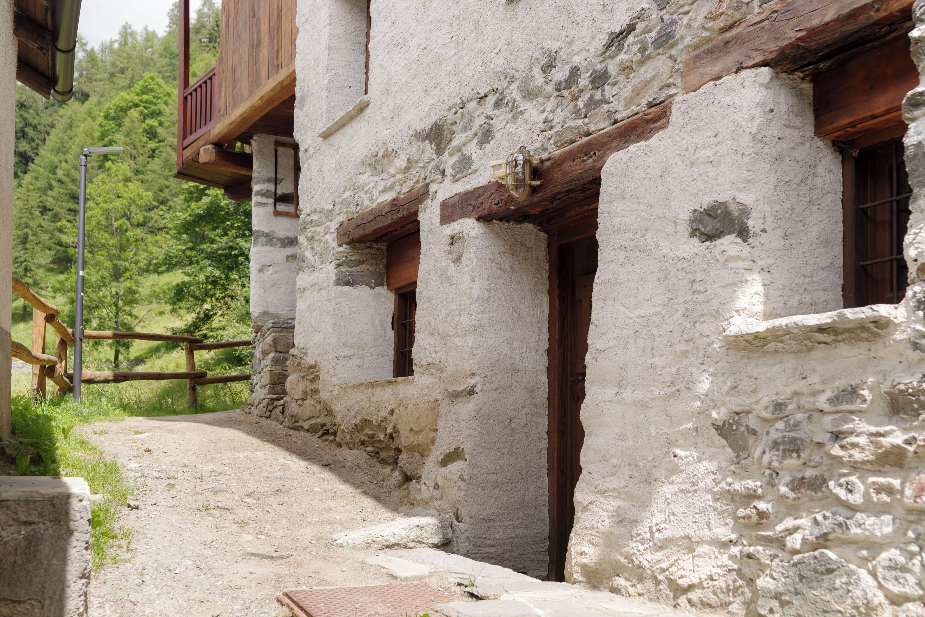 A rustic stone building with wooden balconies and a narrow pathway leading to a door.