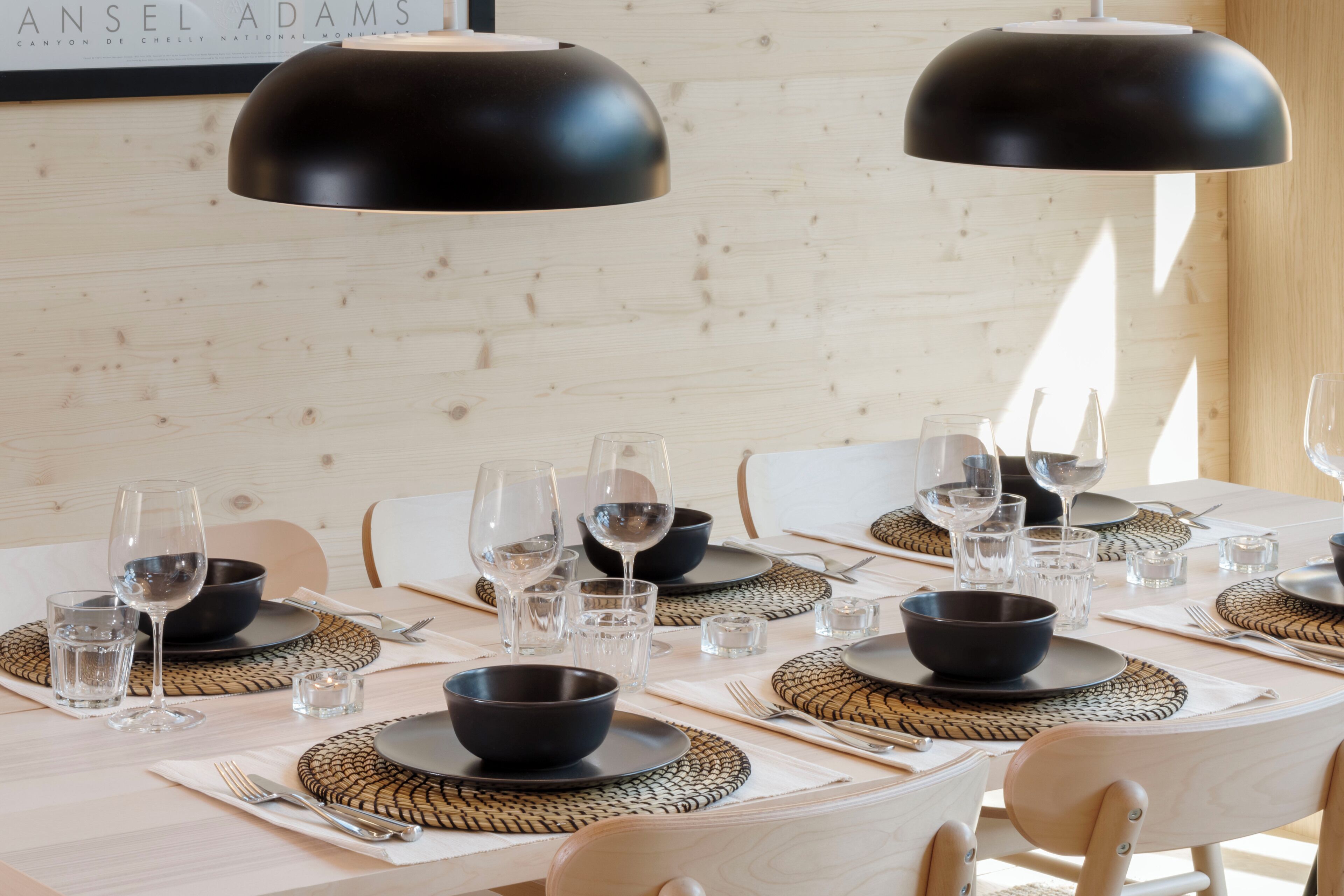 A dining table set with black bowls, plates, and cutlery, with woven placemats and a framed menu above.