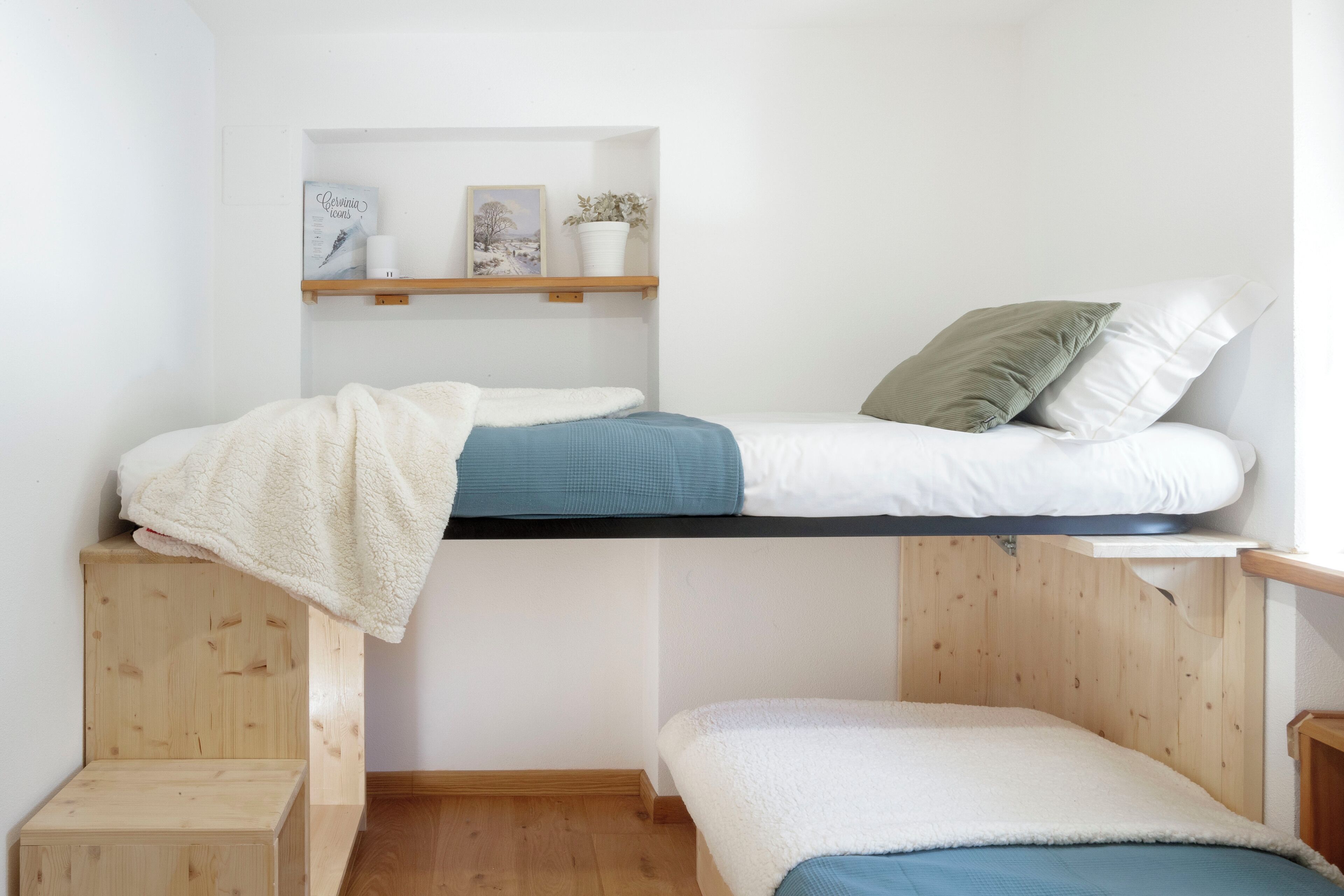 Un lit superposé avec une étagère au-dessus, sur laquelle se trouvent un tableau encadré, une bougie et une plante en pot.