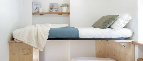 Un lit superposé avec une étagère au-dessus, sur laquelle se trouvent un tableau encadré, une bougie et une plante en pot.