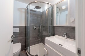 Uma casa de banho moderna com cabine de duche em vidro, lavatório branco e sanita.
