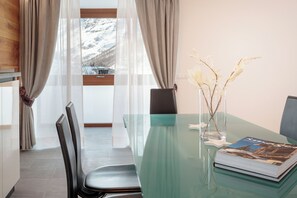 Uma sala de jantar moderna com mesa de vidro, cadeiras, um vaso com galhos e um livro.