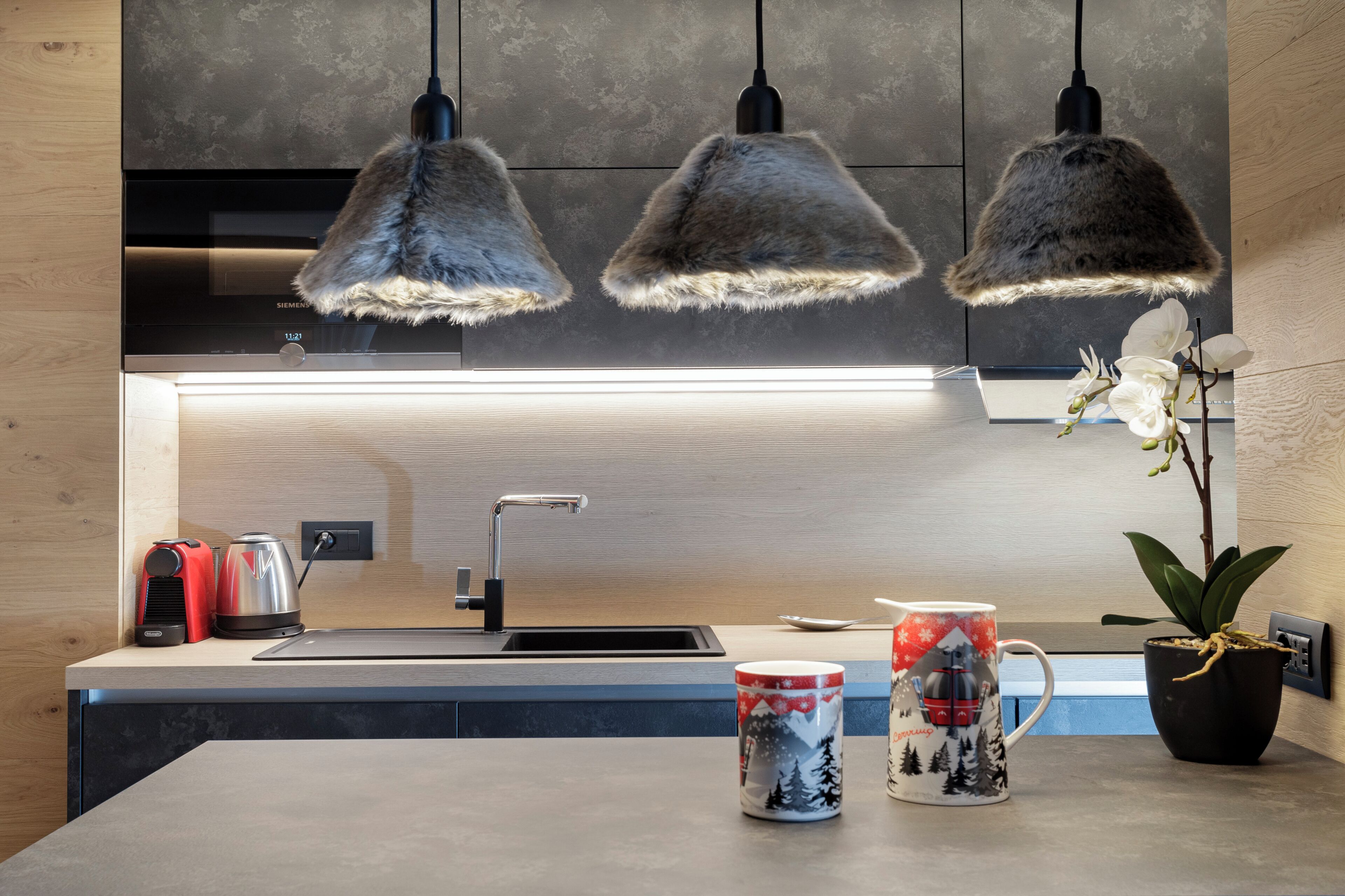 A modern kitchen with pendant lights, a sink, a kettle, a mug, and a potted plant.