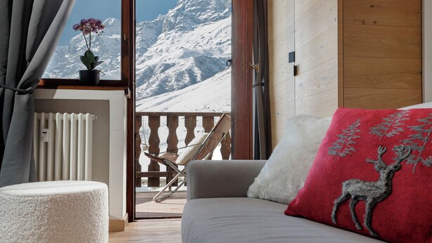 A room with a view of snow-capped mountains, a wooden floor, a white fluffy chair, a sofa with a red pillow, and a potted orchid. - Pandora Mountain View - Central Apartment (Breuil-Cervinia)