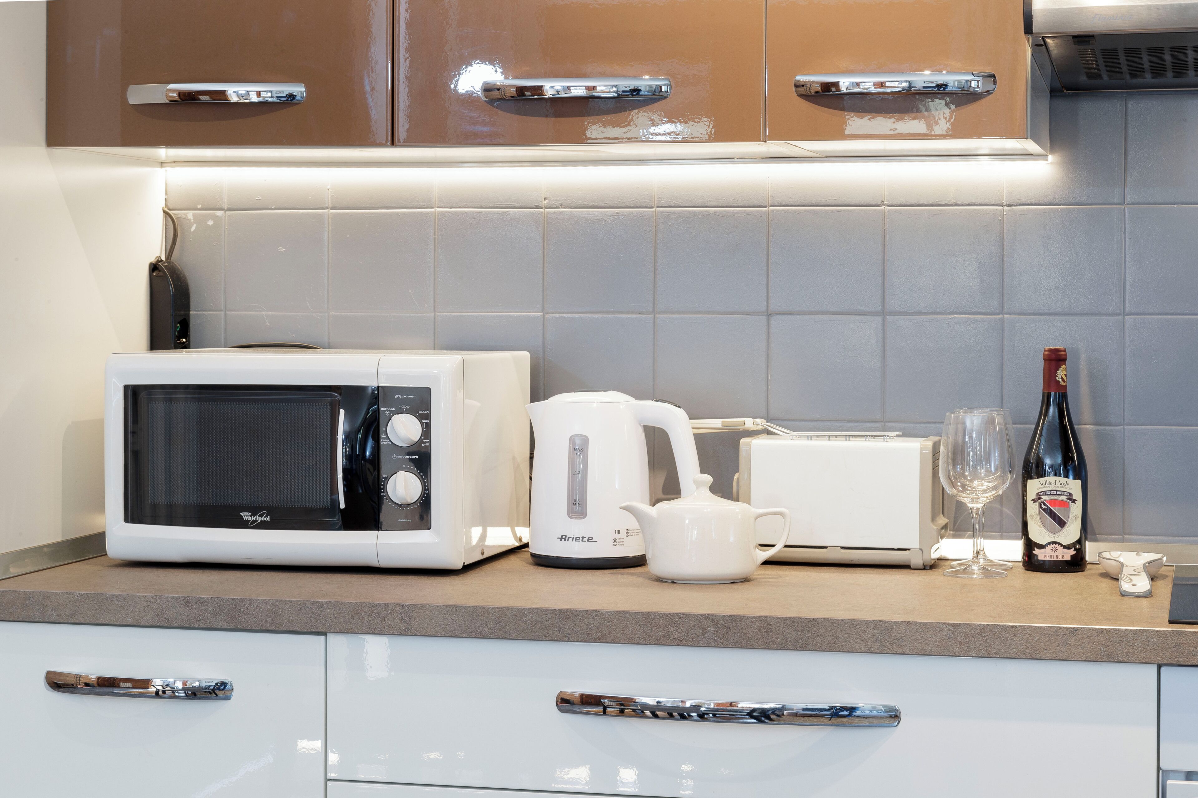 A kitchen with a microwave, toaster, kettle, and wine bottle.