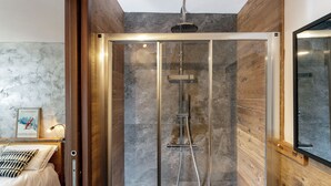 A modern bathroom with a glass-enclosed shower, wooden paneling, and a bed with a headboard.