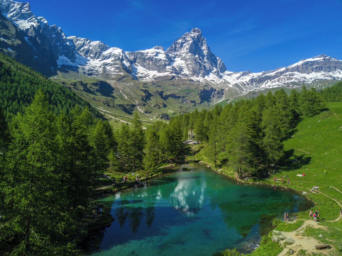 Un paisaje montañoso con un lago cristalino rodeado de bosques densos y cumbres nevadas.