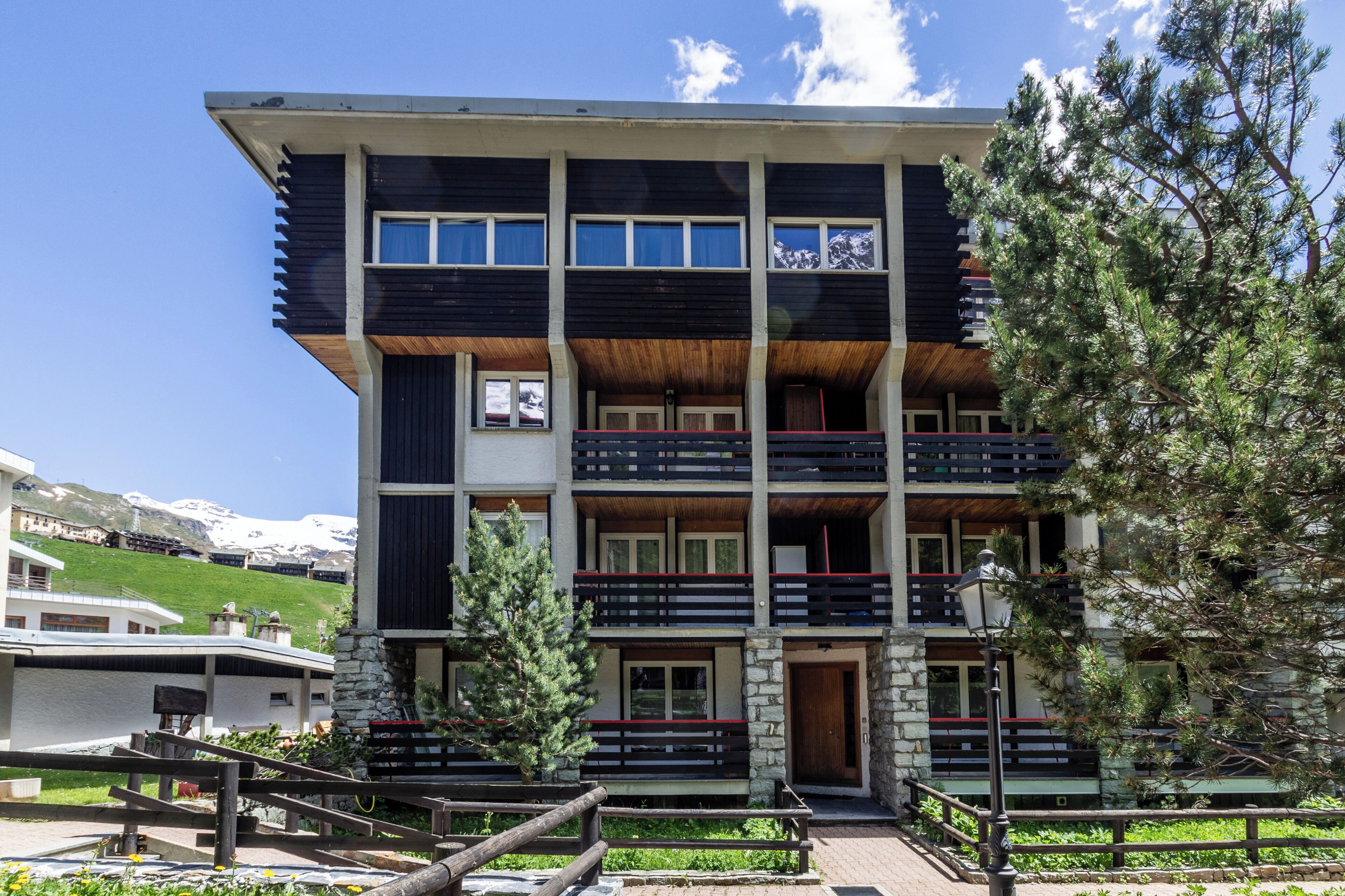 A multi-story building with balconies, a stone facade, and a view of snow-capped mountains.