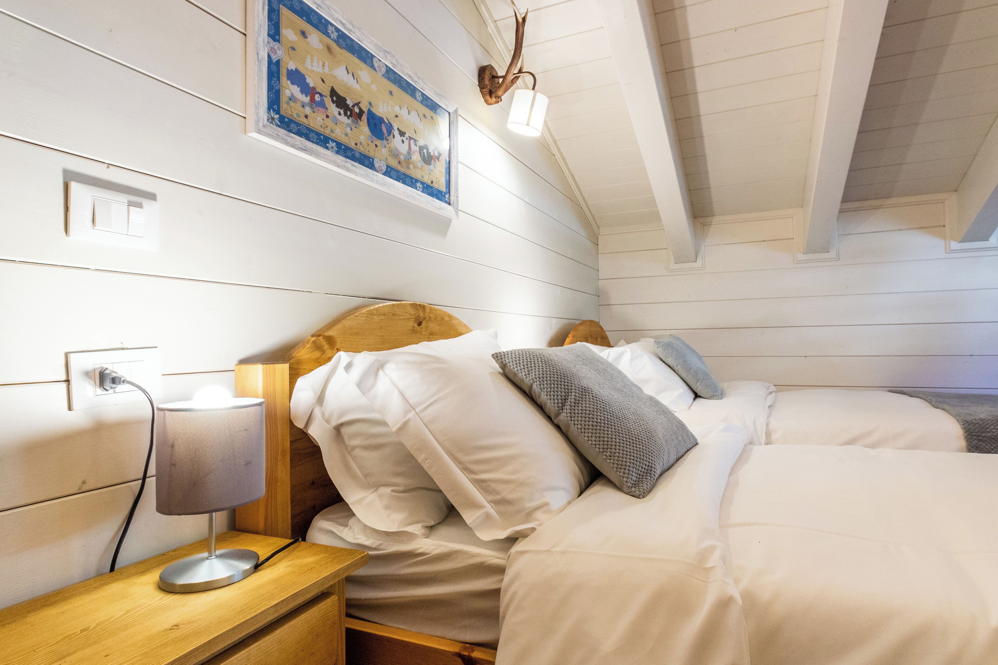 A bedroom with a wooden headboard, a bedside table with a lamp, and a wall-mounted light fixture.