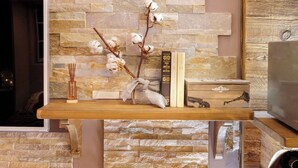 Una habitación con pared de piedra, una mesa de madera con libros y un florero, y un televisor.