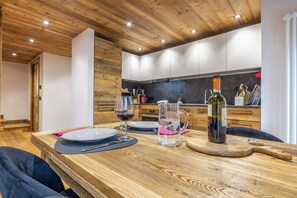 Ein Holztisch gedeckt mit Tellern, Gläsern und einer Flasche, mit einer Küche im Hintergrund.