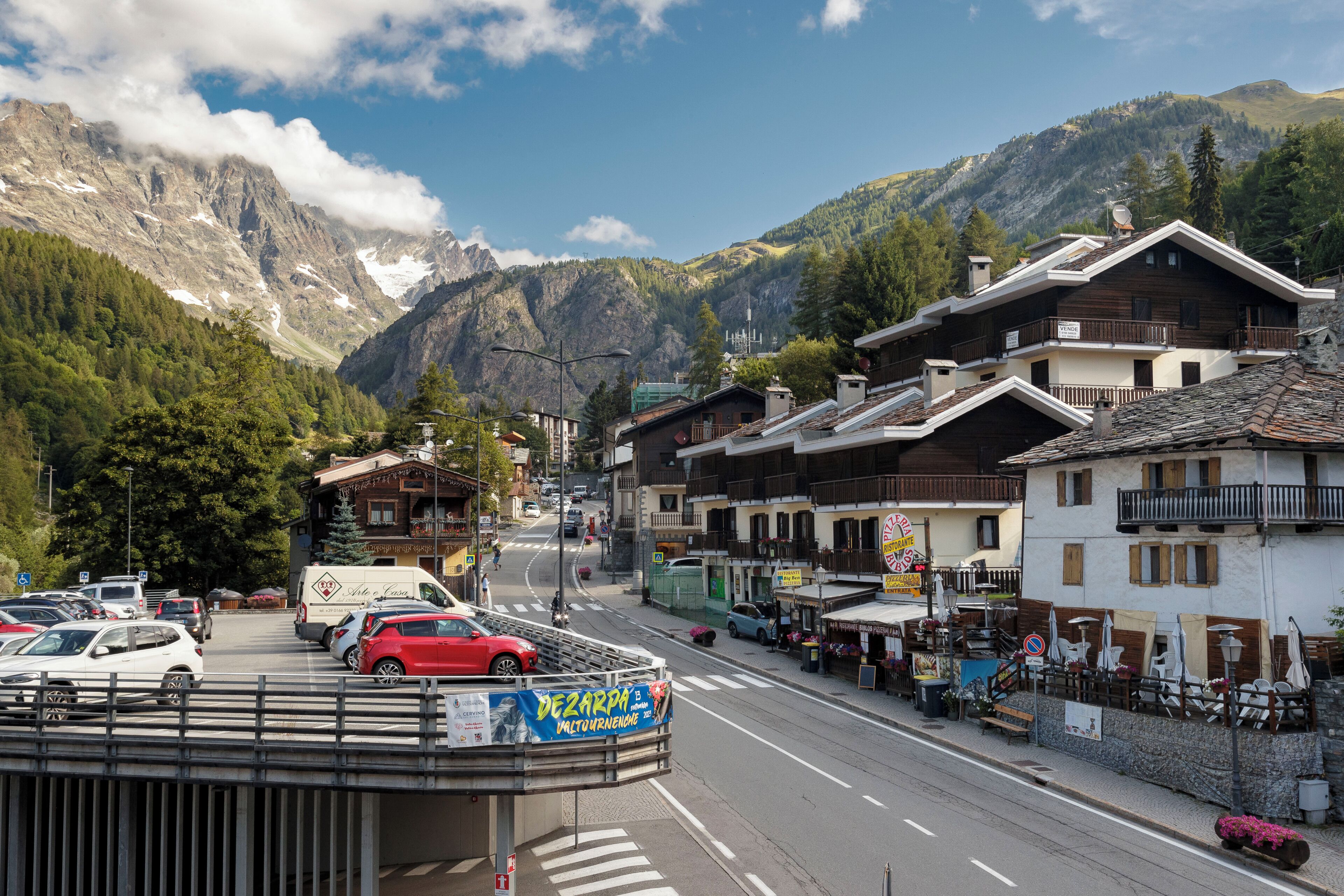 A mountain town with traditional buildings, a street with cars, and a clear view of the mountains in the background.