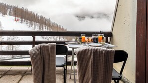 Un balcón con una mesa lista para el desayuno, con vistas a una montaña nevada y un bosque.