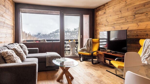 Una sala de estar moderna con un sofá, un sillón, una mesa de centro de vidrio y un televisor de pantalla plana.