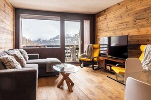 Un salon moderne avec un canapé, un fauteuil, une table basse en verre et un téléviseur à écran plat.