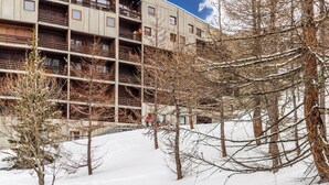 Un edificio de varios pisos con el suelo cubierto de nieve, árboles desnudas y un cielo despejado.