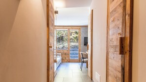 Um corredor estreito com paredes de madeira, chão de azulejos e vista para uma floresta através de uma porta de vidro.
