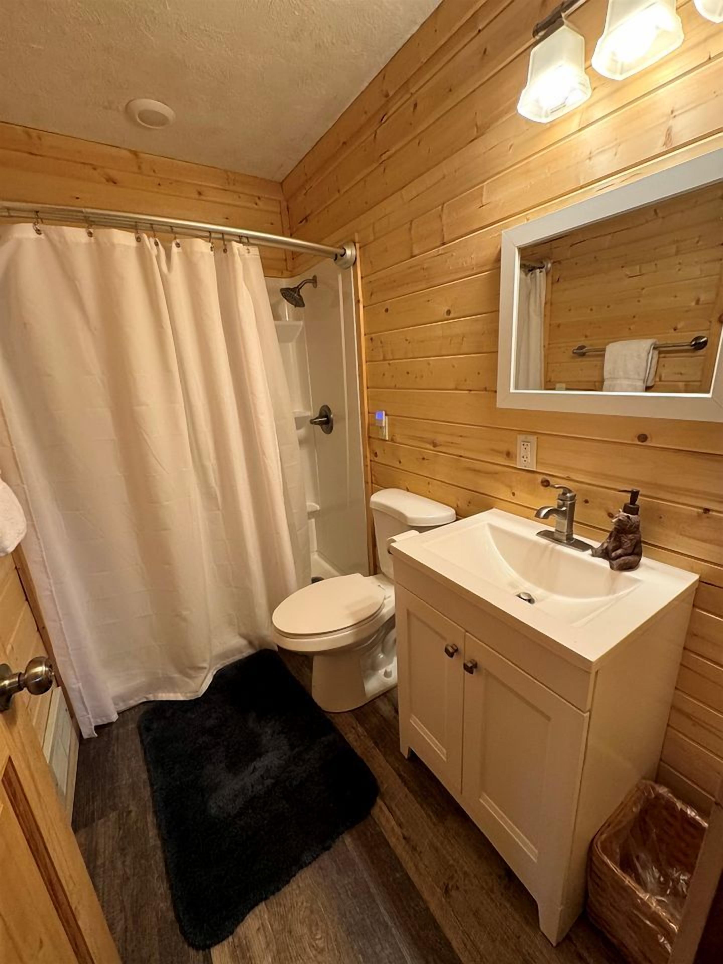 A wooden-paneled bathroom with a shower curtain, toilet, sink, and mirror.