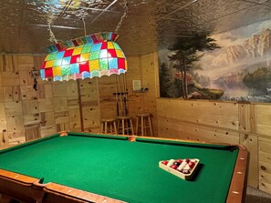 Une table de billard, un lampadaire coloré suspendu au plafond, des murs en bois et une fresque représentant un paysage de montagne.