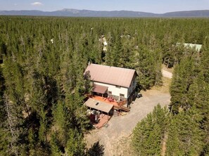 A cabin surrounded by dense forest, with a dirt driveway leading to the entrance. - Incredible Cabin Perfect for Family Reunions near Yellowstone, Idaho (Island Park)