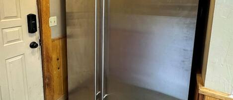 A stainless steel refrigerator in a kitchen with a wooden door frame and a tiled floor.