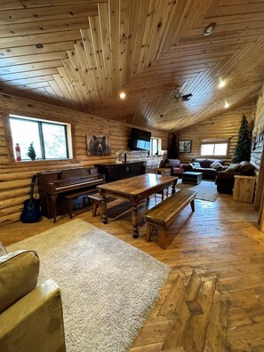 L'intérieur d'une cabane en rondins, avec une table à manger en bois, des bancs, un piano, une cheminée et un coin salon confortable.