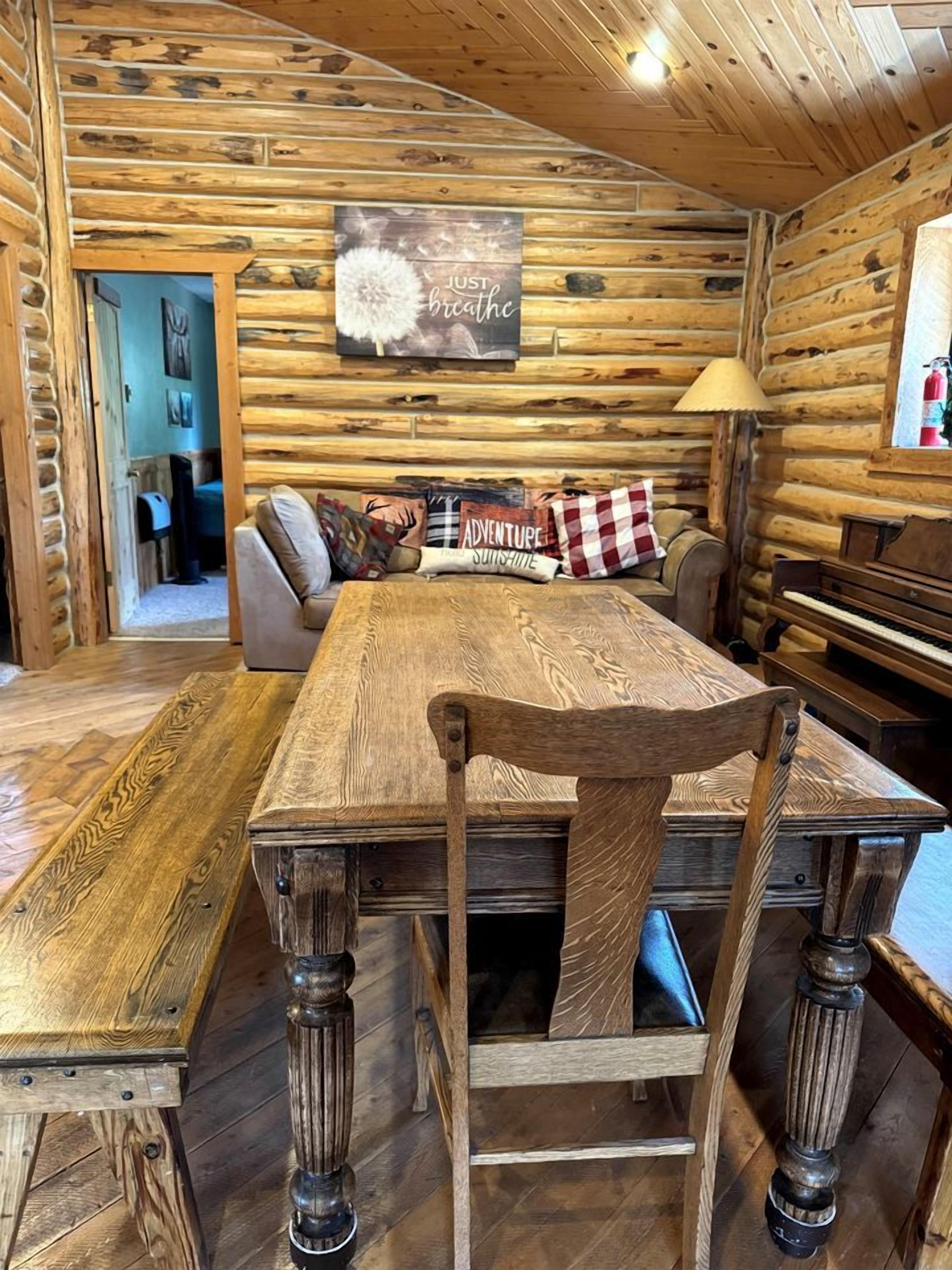 Un intérieur rustique en bois, avec une table à manger, des chaises et un canapé agrémenté d’une pancarte sur laquelle on peut lire : « Respirez ».