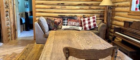 Un intérieur rustique en bois, avec une table à manger, des chaises et un canapé agrémenté d’une pancarte sur laquelle on peut lire : « Respirez ».
