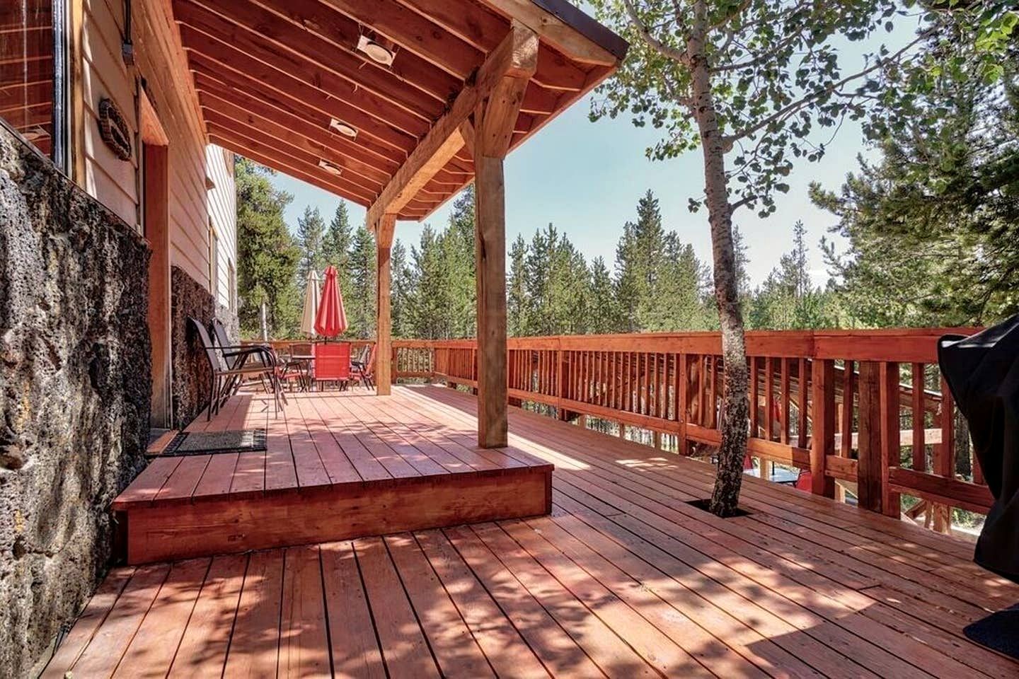A wooden deck with a covered seating area, surrounded by trees.