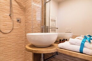 Un baño con un lavamanos blanco de pedestal, un box de ducha de cristal y un mueble de tocador de madera con toallas.