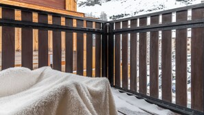 En træbalkon med en hvid, lodden genstand på den, og et snedækket bjerg i baggrunden.