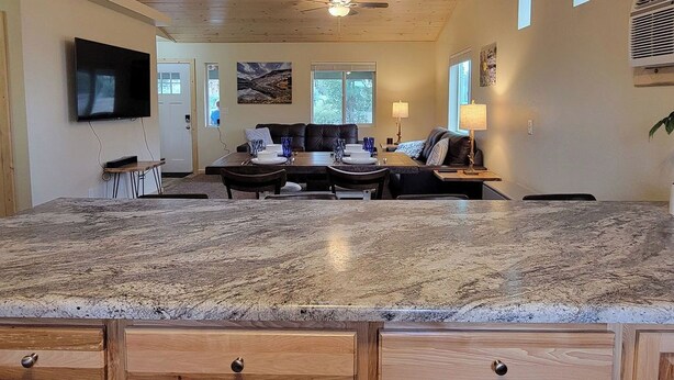 A spacious kitchen with a granite countertop, wooden cabinets, a ceiling fan, and a dining area with a table set for four. - Fantastic cabin retreat for 6 with 2 bathrooms and AC in cozy Heber-Overgaard (Heber-Overgaard)