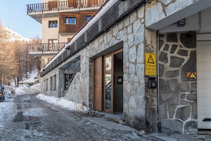 A stone building with a metal balcony, a warning sign, and a snow-covered street.