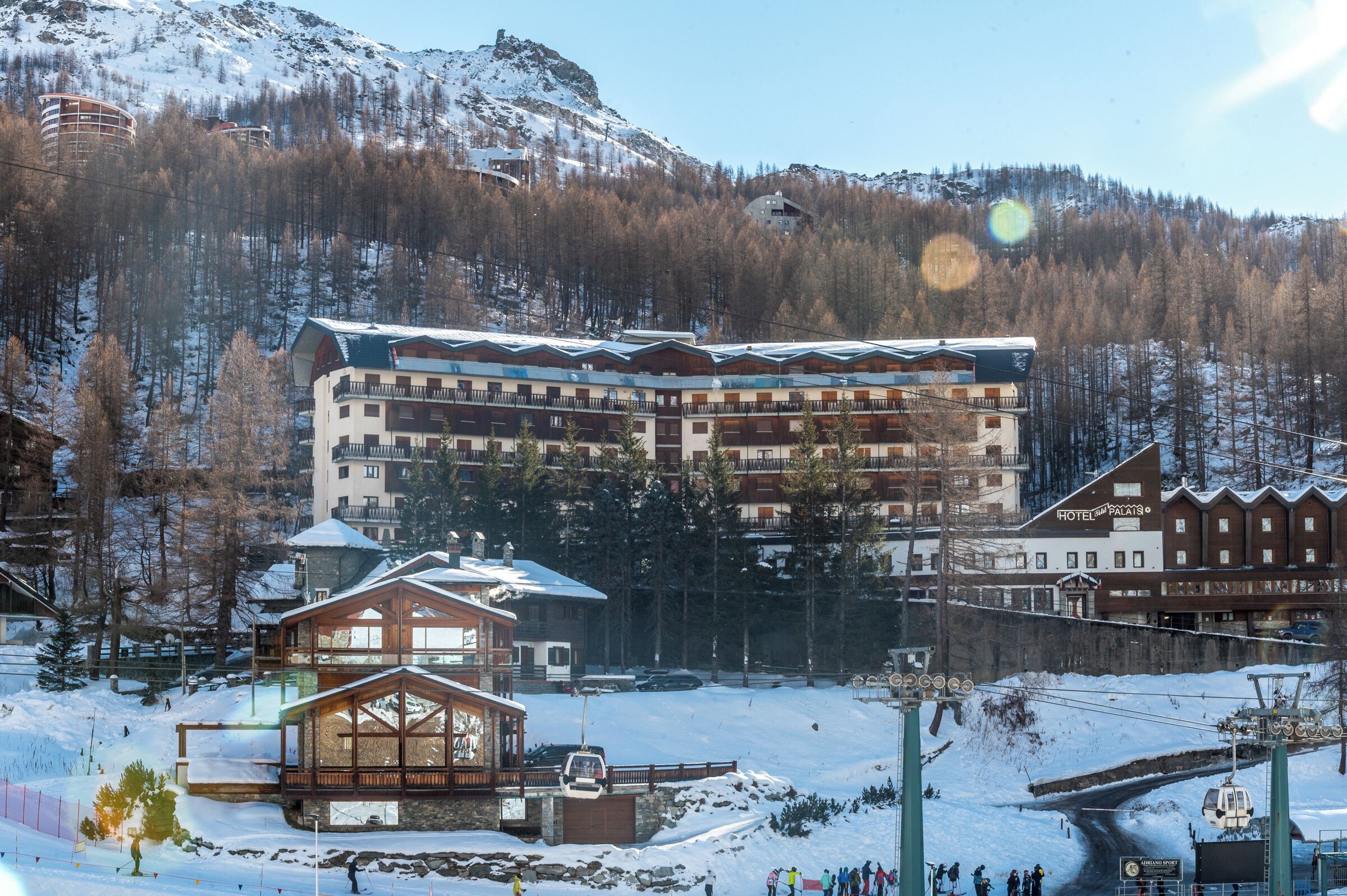 Un hotel de varios pisos con balcones, un telesilla y montañas al fondo.