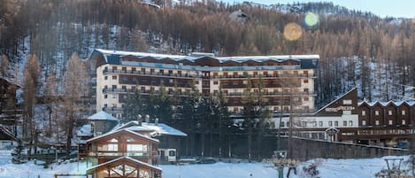 Un hotel de varios pisos con balcones, un telesilla y montañas al fondo.